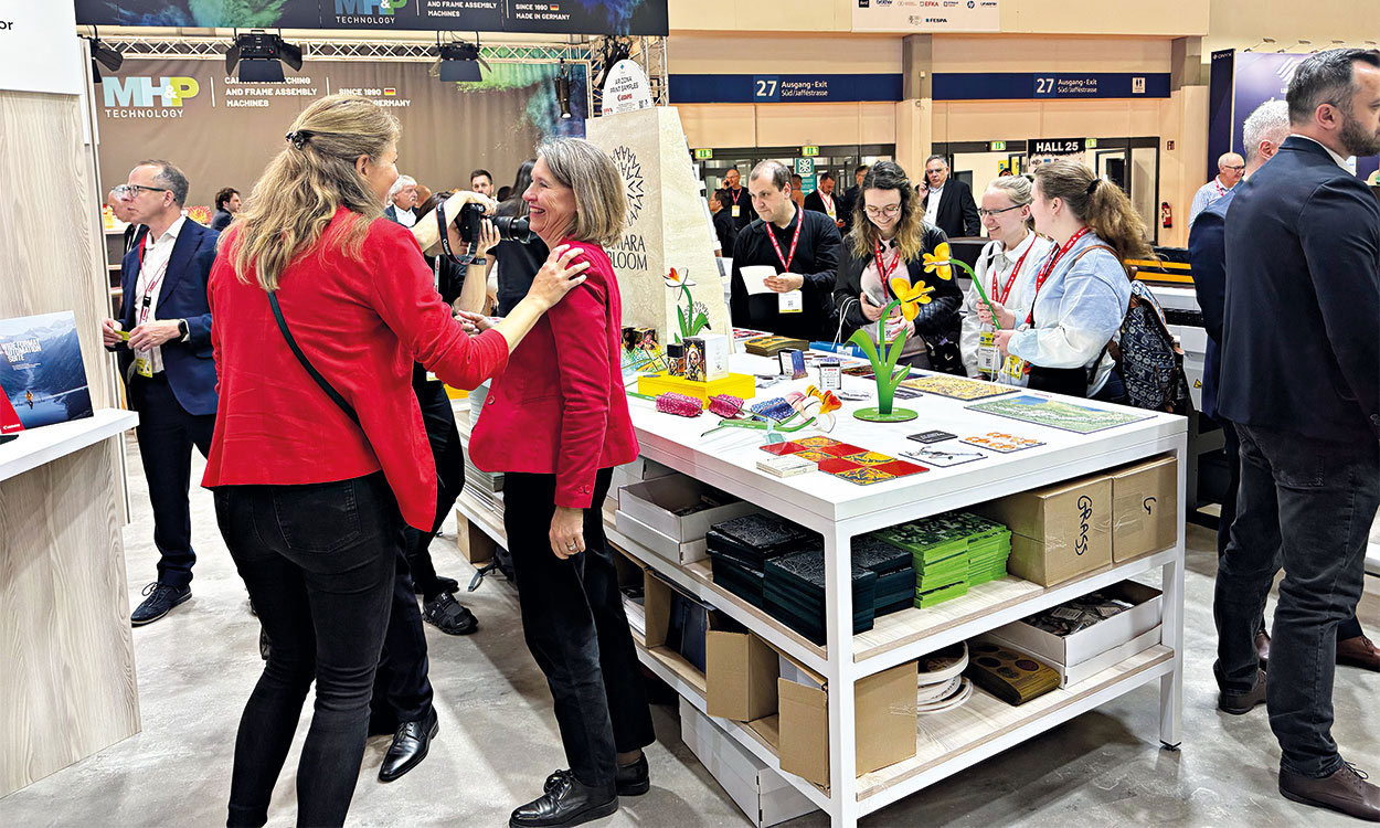 Zwei Besucherinnen gut gelaunt an Messestand. Weitere Besucher im Hintergrund.