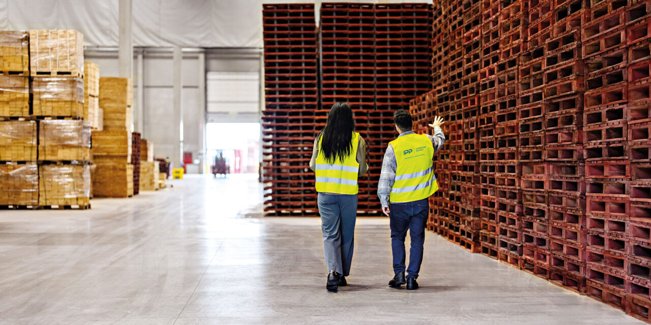 Zwei Personen laufen durch Lager mit Paletten.