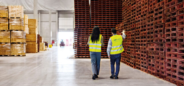 Zwei Personen laufen durch Lager mit Paletten.