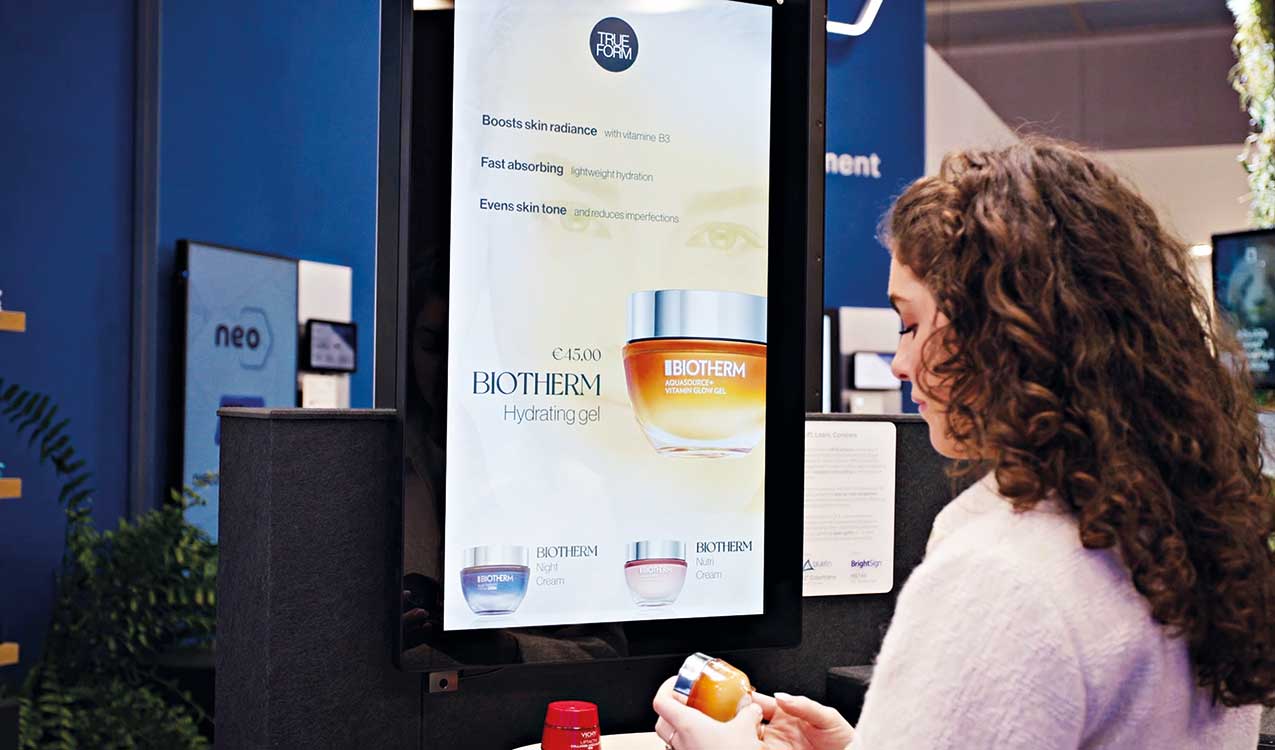 Frau schaut sich Parfümflasche an, während weitere Produktinfos auf Screen gezeigt werden.