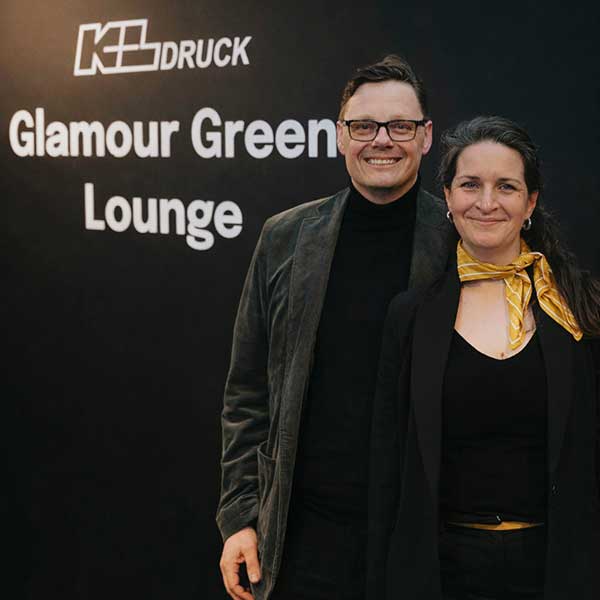 Christian Schmäling und Nina Schiborr von KL Druck vor Schwarzer Wand mit Aufschrift "KL Druck Glamour Green Lounge."