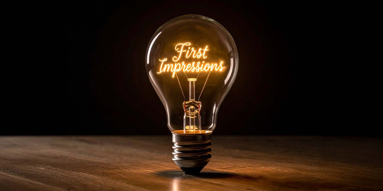 Glühbirne auf Tisch mit Glühfaden mit den Worten "First Impressions"